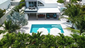 Ein modernes Haus mit Pool, überdachter Terrasse und üppiger Bepflanzung.