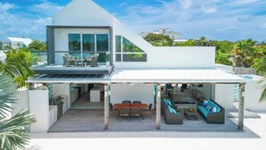 Ein modernes Haus mit Pool, Sitzgelegenheiten im Freien und einer überdachten Terrasse.