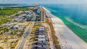 An aerial view of a coastal area with a long beachfront, a road running parallel to the beach, and several buildings including a hotel with multiple floors and a pool. - NEW Rental!!! Viviana 1~Beach Lovin - Private Pool Beach Front Home (Perdido Key)