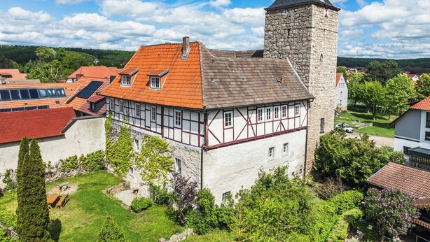 A traditional half-timbered house with a stone tower, surrounded by lush greenery and other residential buildings. - Group meetings and overnight stays in historic walls in the heart of Germany (Großbodungen)