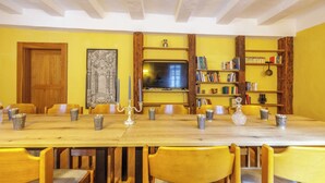 A dining area with a long wooden table, yellow chairs, a bookshelf, and a television. - Group meetings and overnight stays in historic walls in the heart of Germany (Großbodungen)