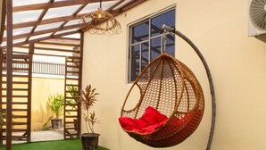 A hanging chair with red cushions in a covered outdoor area with artificial grass and potted plants. - Cozy 2BED w/ Private Cinema @ Bodija, Ibadan (Ibadan)