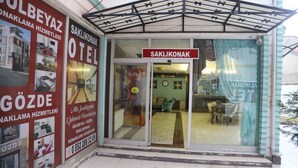 L’entrée d’un hôtel, avec une enseigne indiquant « SAKLIKONAK HOTEL », un espace de réception et un réfrigérateur à boissons Coca-Cola à l’intérieur.