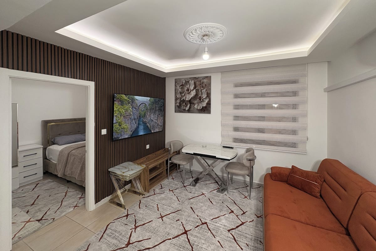 A modern living room with a bed, TV, desk, and orange sofa.