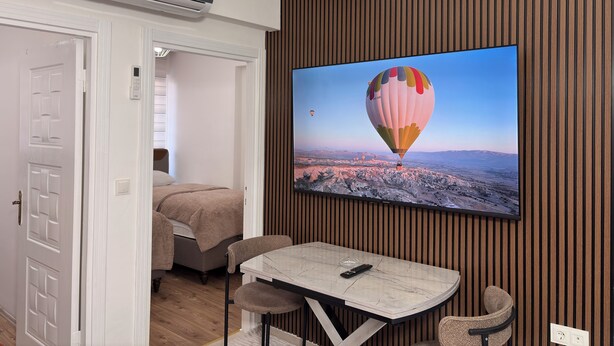 Une chambre moderne équipée d’un téléviseur mural diffusant des images d’une montgolfière, d’une table à manger avec des chaises, d’un lit et d’un climatiseur.