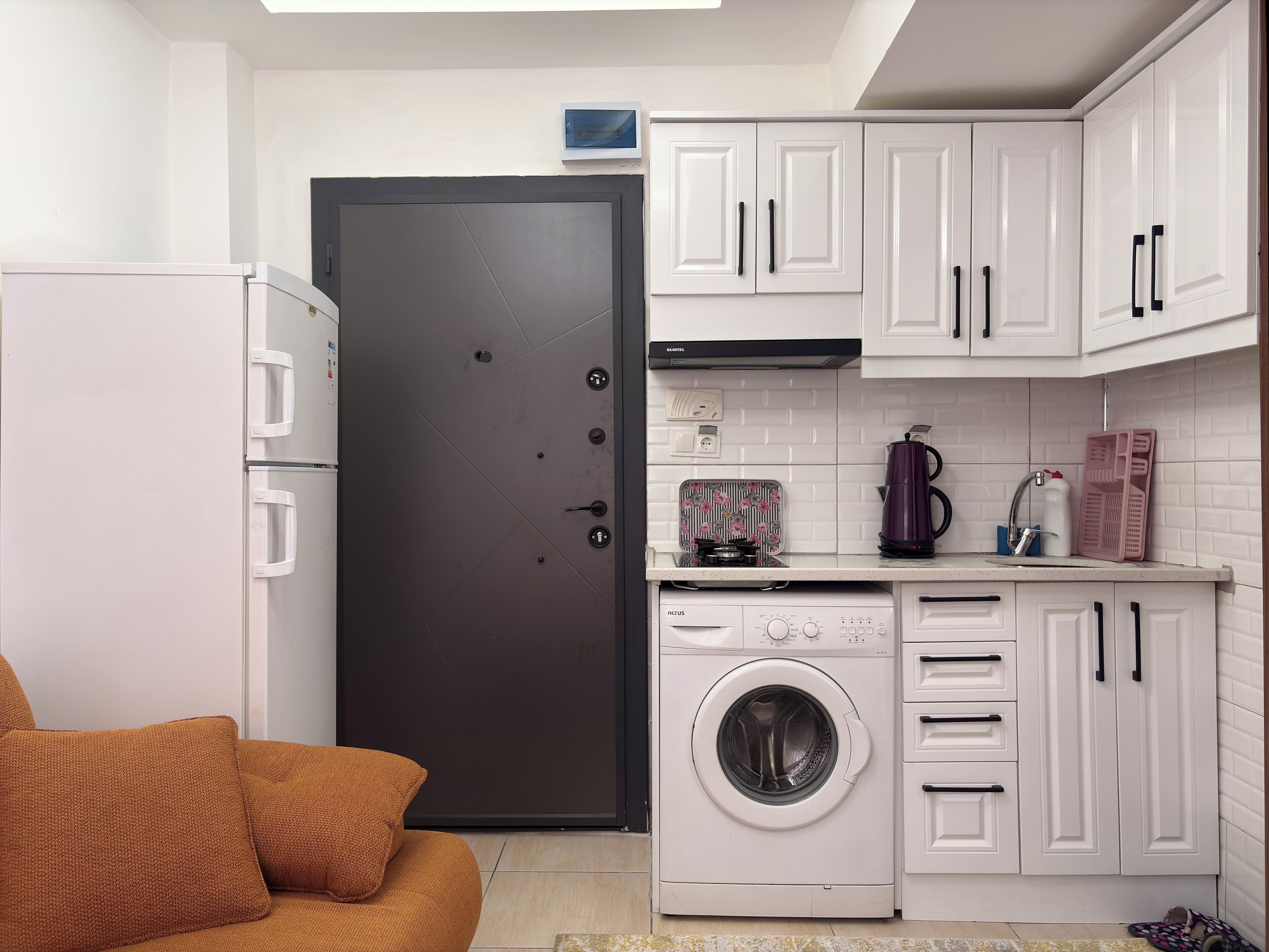 A compact kitchen with a washing machine, a coffee maker, and a refrigerator.