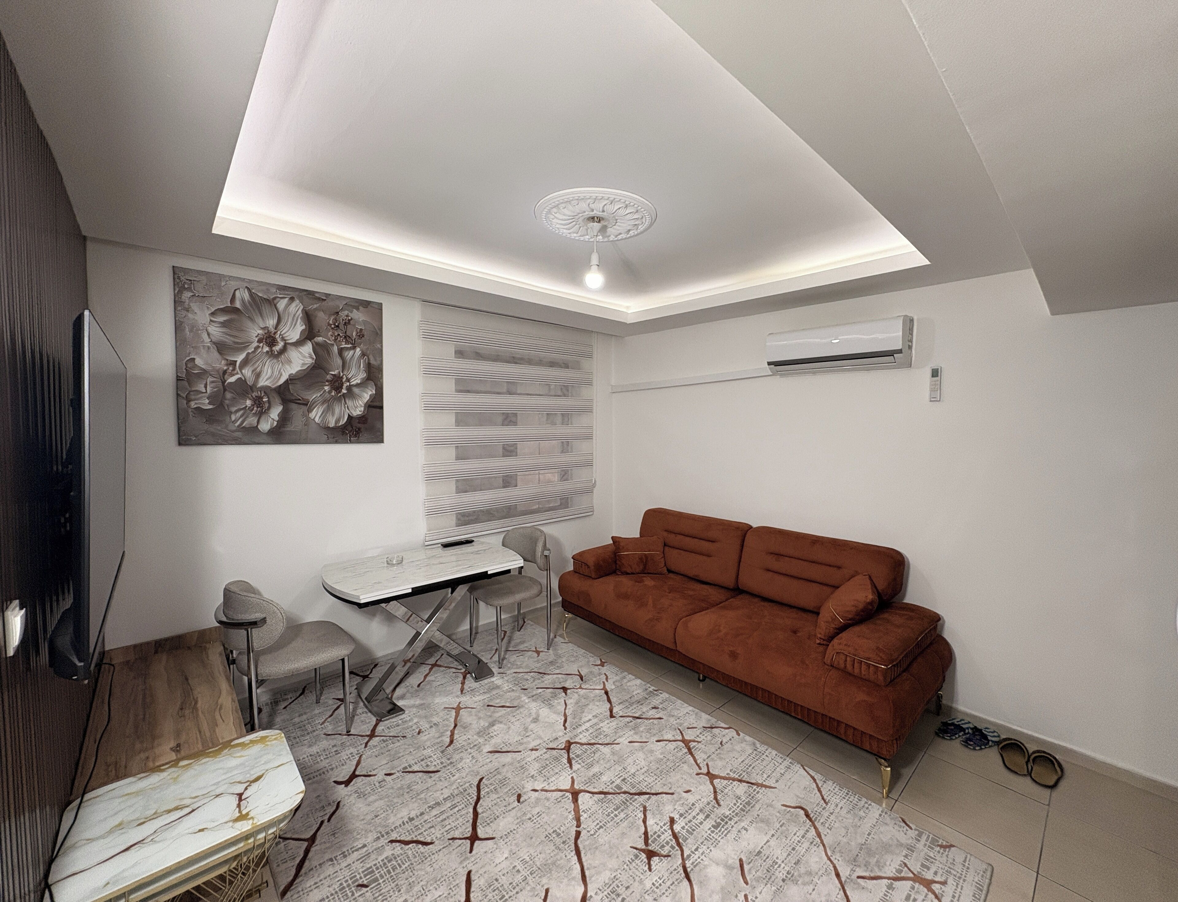 A modern living room with a brown sofa, a dining table, a TV, and a ceiling fan.