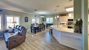 Een ruime woonkamer met een leren bank, een eethoek met een houten tafel en een keuken met een groot eiland en hanglampen.
