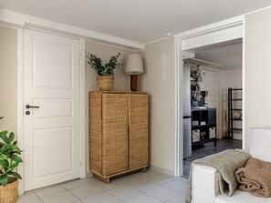 A hallway with a white door, wicker cabinet, and a lamp.
