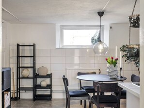 A modern kitchen with a dining area, featuring a round table, chairs, a hanging light fixture, and a window.