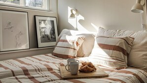 A neatly made bed with striped bedding, a tray with croissants and a mug, and framed pictures on the wall.