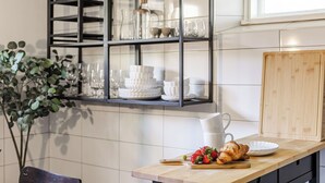 A kitchen with a wooden countertop, a shelf with glassware, and a potted plant.