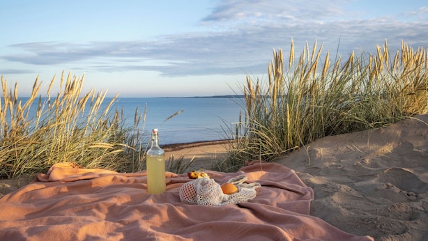 A beach scene with a blanket, a bottle, and some snacks.
