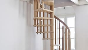 A modern room with a spiral wooden staircase, a cushioned chair, and a window providing natural light. - 1809 Villa (Santorini)
