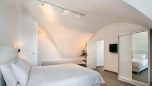 A modern bedroom with a large bed, a walk-in closet, and a television on the wall. - 1809 Villa (Santorini)