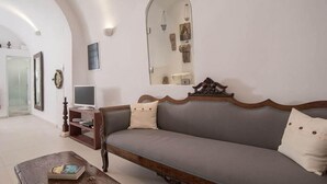 A living room with a sofa, a coffee table, a TV, and a mirror on the wall. - Dimitrios Cave House (Santorini)