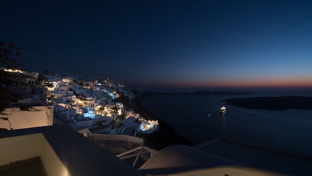 A coastal town at night with white buildings and a view of the sea. - Dimitrios Cave House (Santorini)