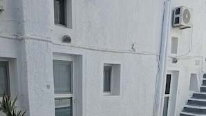 A swimming pool with a white exterior wall, a small window, and a potted plant. - Leta Santorini (Santorini)