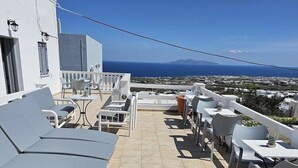 A rooftop terrace with sun loungers and tables, offering a view of the sea and distant mountains. - Leta Santorini (Santorini)