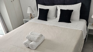 A neatly made bed with a white duvet, black pillows, and rolled white towels. - Leta Santorini (Santorini)