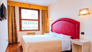 A hotel room with a large bed, a window with a view of a building, a red headboard, and two wall-mounted lamps. - The Dome - Panoramic Rooms (Ferrara)