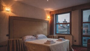 A hotel room with a large bed, a view of a cityscape through a window, and a red carpeted floor. - The Dome - Panoramic Rooms (Ferrara)