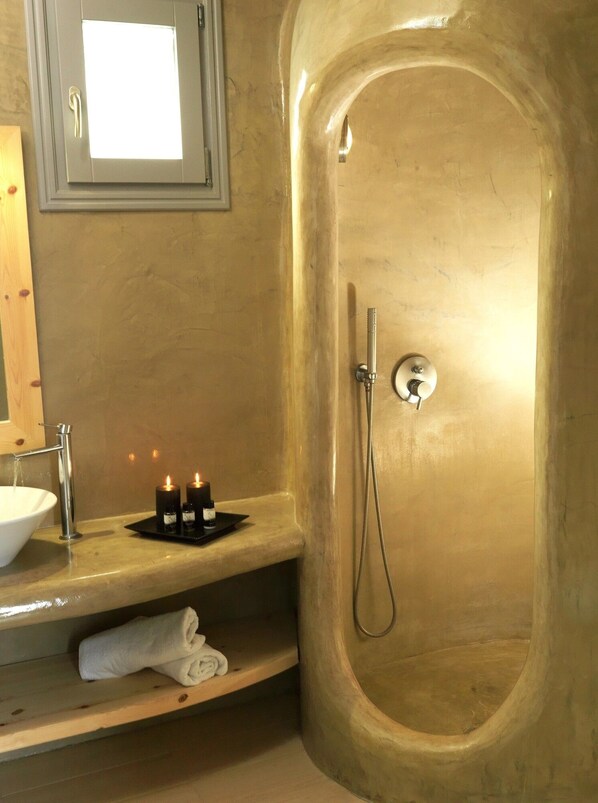 A bathroom with a bathtub, a sink, and a mirror. There are candles on the sink. - San Marino Suites (Santorini)