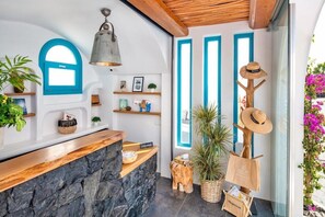 A reception area with a stone counter, blue-framed windows, and a wooden ceiling. - San Marino Suites (Santorini)