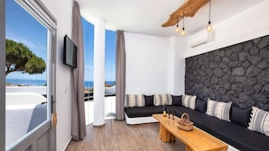 A modern living room with a stone wall, a black sofa with patterned cushions, a wooden coffee table, and a television mounted on the wall. - San Marino Suites (Santorini)