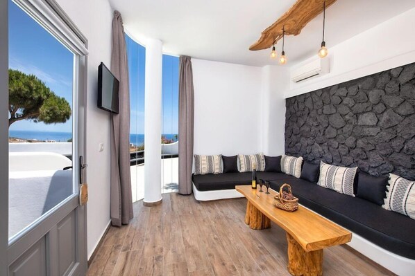 Ein modernes Wohnzimmer mit Steinwand, einer schwarzen Couch mit gemusterten Kissen, einem Holztisch und einem an der Wand montierten Fernseher.