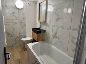 A modern bathroom with a marble-tiled wall, a white toilet, a wooden vanity, and a freestanding bathtub. - Peaceful stay in Trouville, close to the beach (Trouville-sur-Mer)