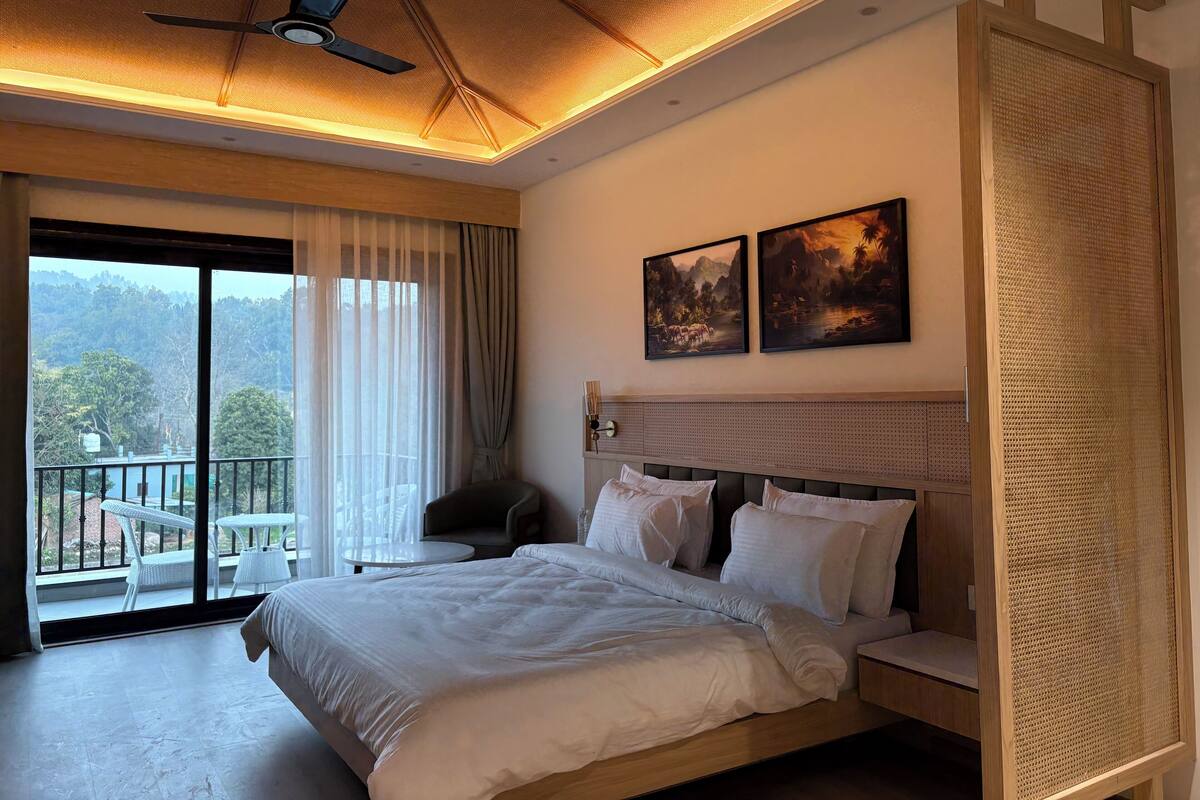 A hotel room with a large bed, a ceiling fan, and a balcony with outdoor furniture.