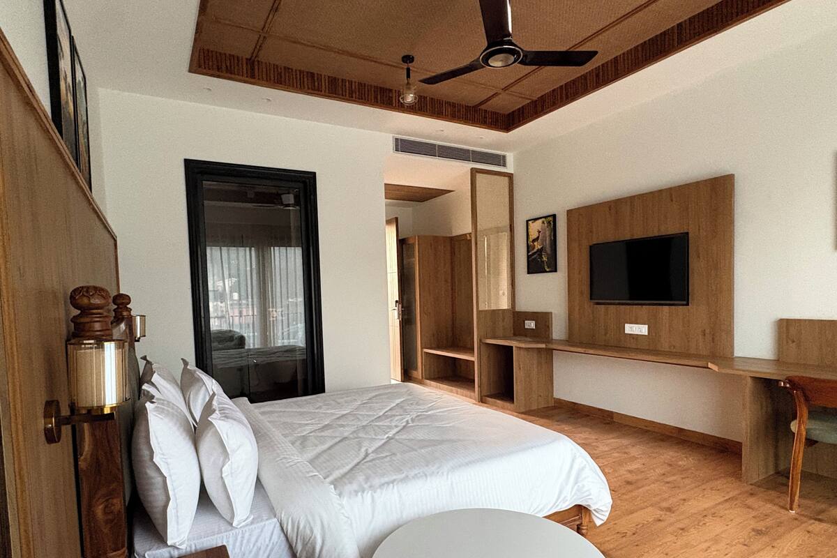 A hotel room with a bed, a round table, a TV mounted on the wall, and a ceiling fan.