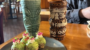 A dining table with a plate of food, a decorative vase, and a drink in a tiki mug. - Corbett Anandavana (Ramnagar)