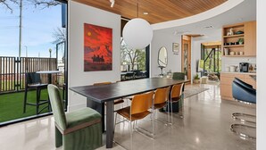 A modern kitchen with wooden cabinets, a dining area with a large table and chairs, and a view of the outdoors. - Architectural Gem w/ Rooftop Terrace + Heated Pool (Austin)