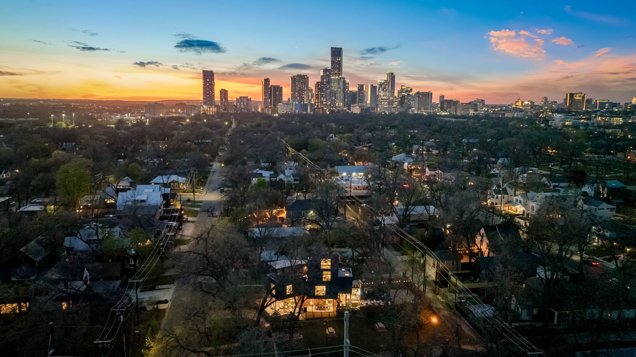An aerial view of a cityscape at dusk with a prominent skyline, residential areas, and a mix of modern and traditional architecture.
