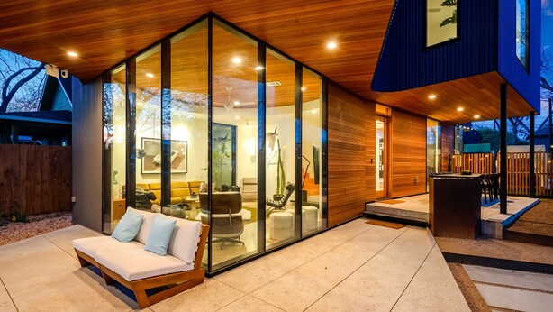 A modern house with a glass-enclosed living area, a wooden deck, and a patio with a sofa. - Architectural Gem w/ Rooftop Terrace + Heated Pool (Austin)