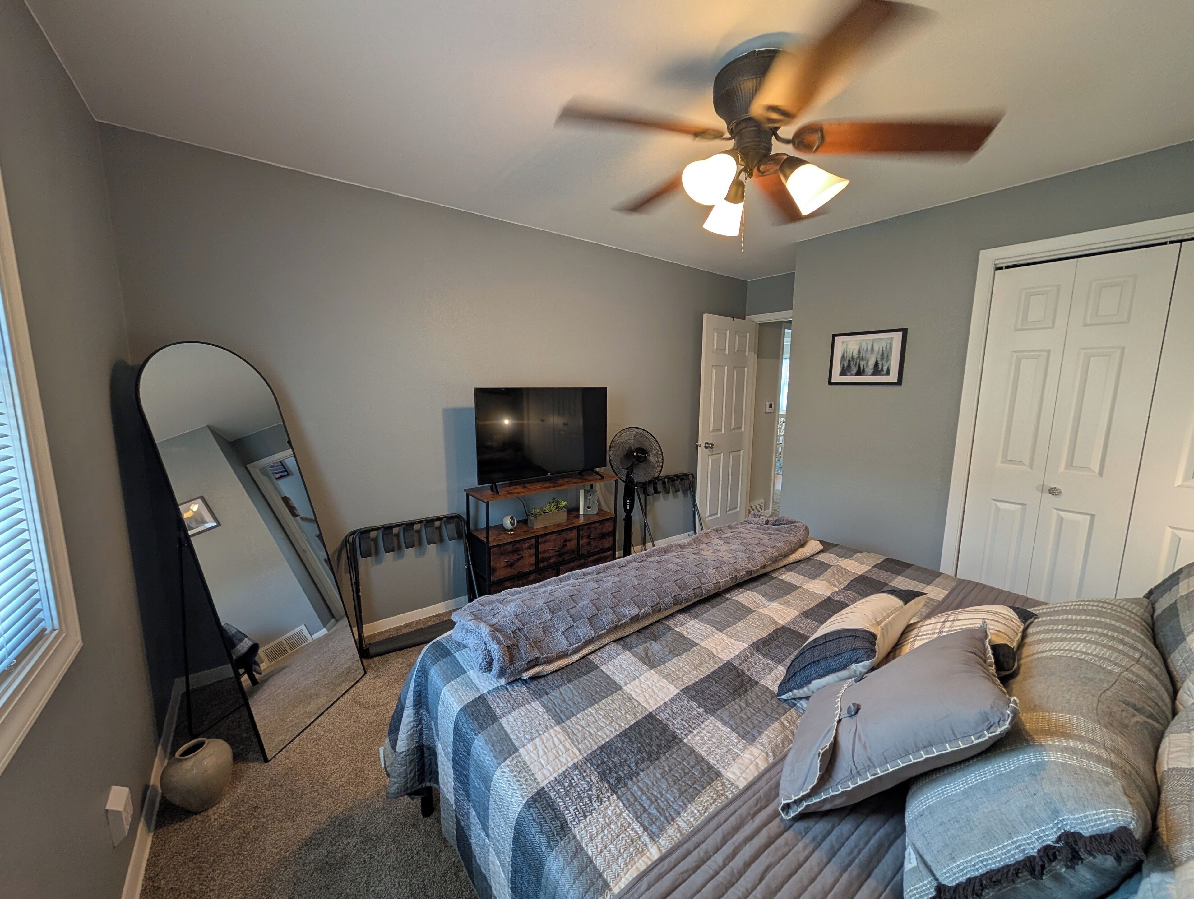 A bedroom with a bed, a ceiling fan, a TV, a dresser, and a door.