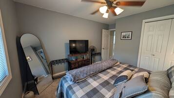 A bedroom with a bed, a ceiling fan, a TV, a dresser, and a door.