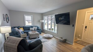 Un salon avec un canapé, un pouf et un téléviseur fixé au mur.
