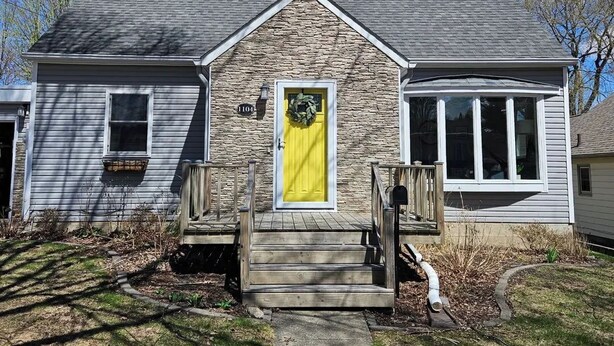 Une maison avec une façade en pierre, une porte d’entrée jaune et le numéro « 1104 » inscrit sur le mur.