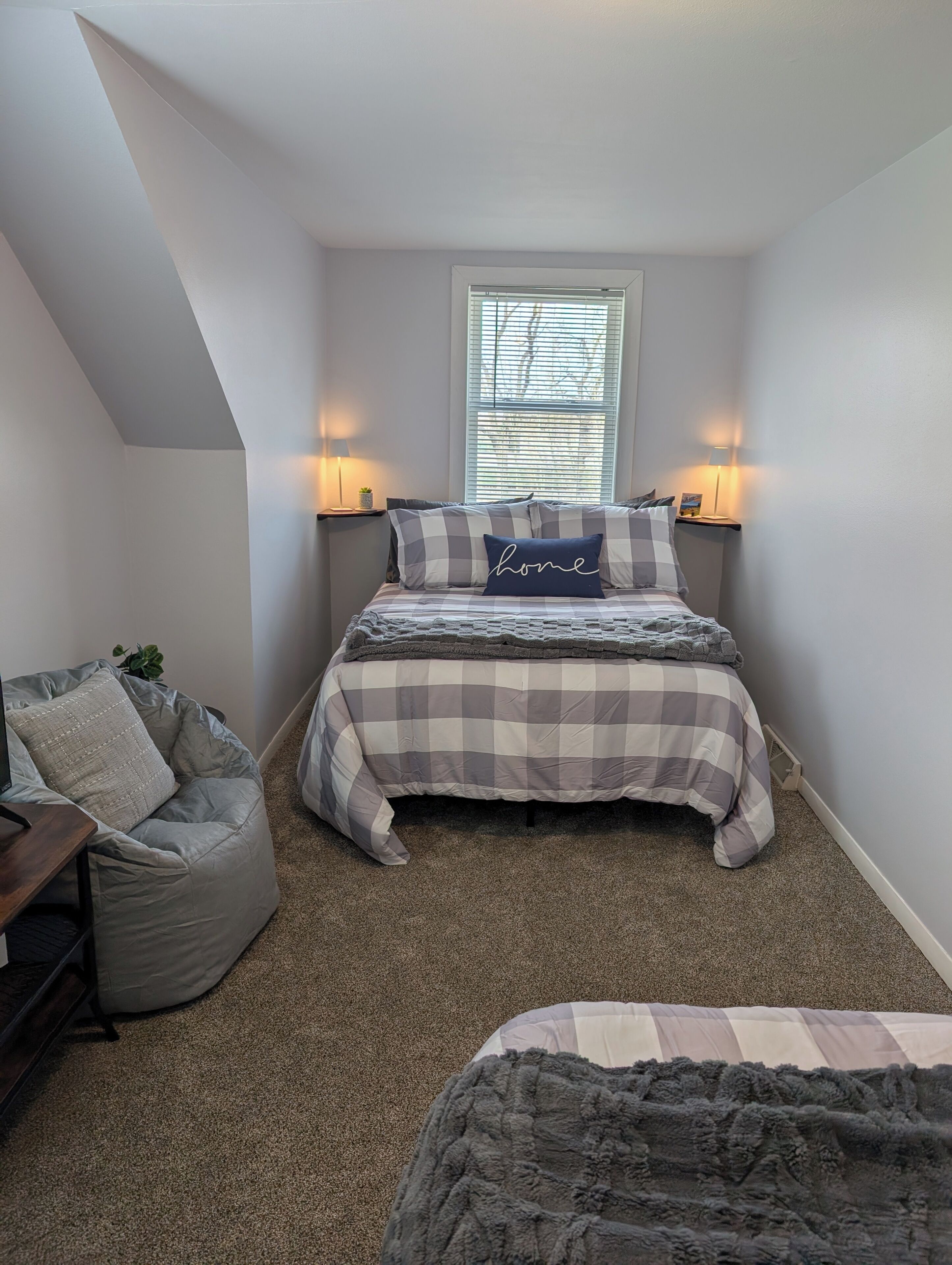 A bedroom with a bed, a chair, a window, and two bedside lamps.