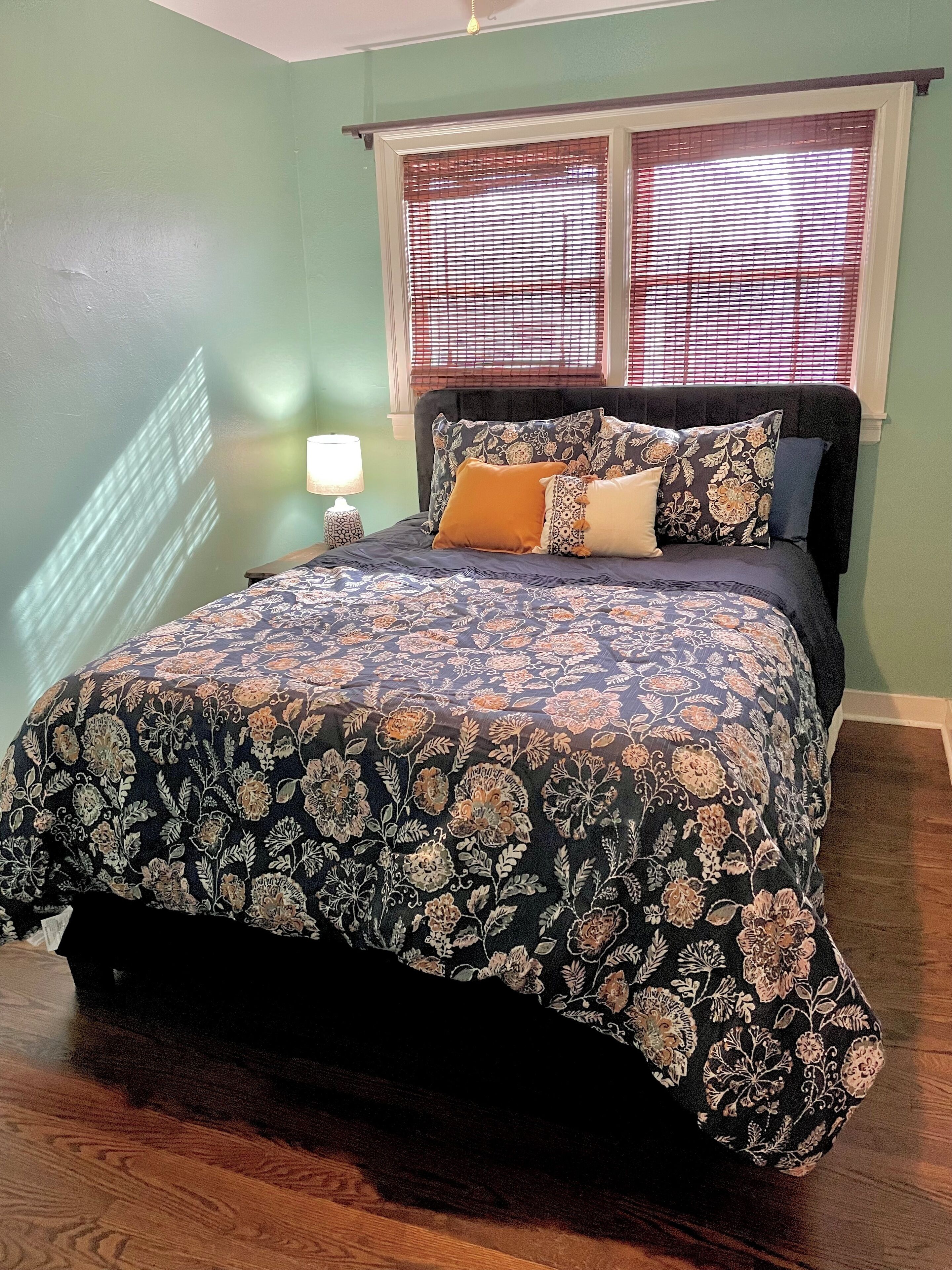 Un dormitorio con cama, mesita de noche, lámpara y ventana con persianas.