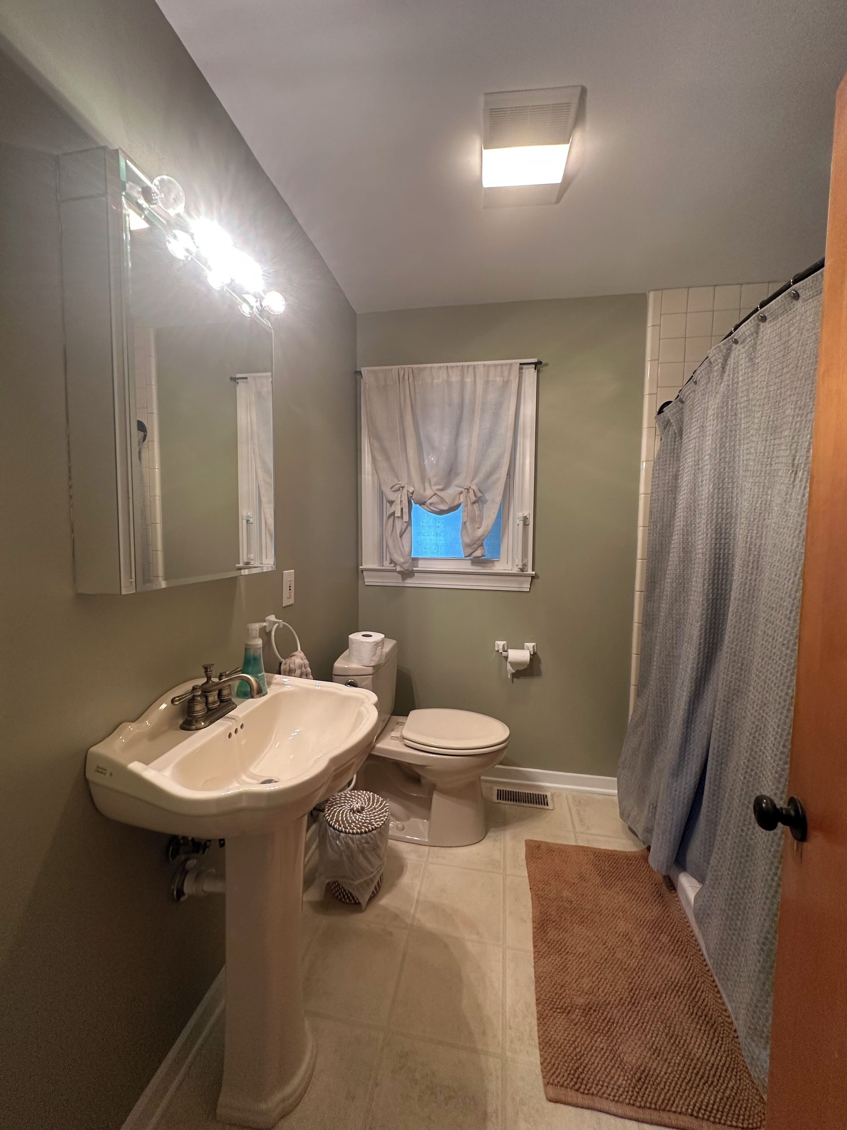 A bathroom with a pedestal sink, toilet, and a window with curtains.