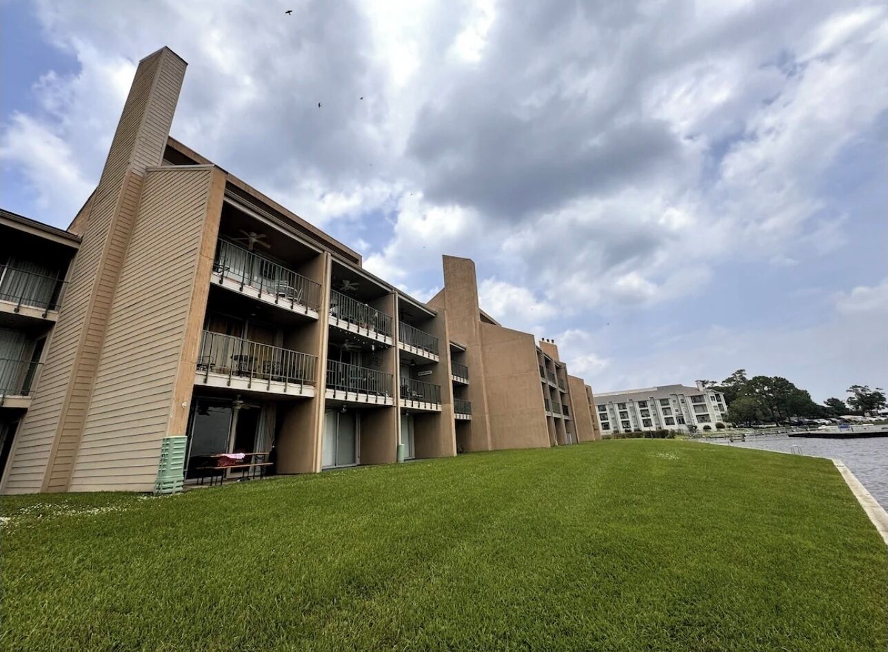 Un edificio de varios pisos con balcones, un césped y una masa de agua al fondo.