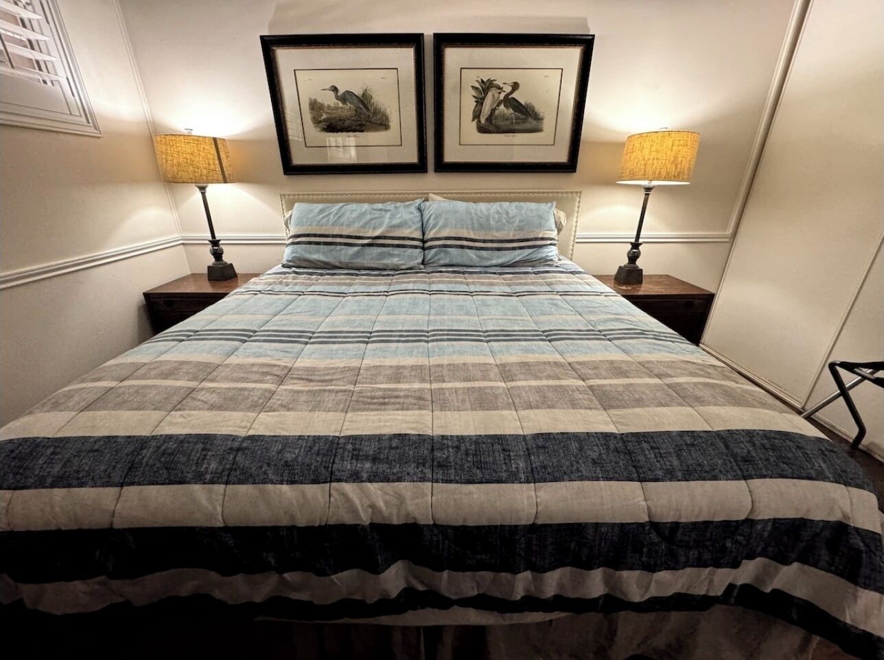 A neatly made bed with a striped bedspread, two bedside lamps, and two framed pictures on the wall.