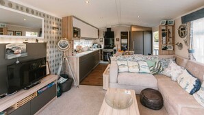 A compact living space with a kitchenette, a sofa, a coffee table, and a television. - 'Serenity' A Tranquil & Peaceful Retreat set in a Cornish country park (Relubbus)