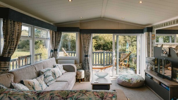 A cozy living room with a sofa, a coffee table, and a TV stand. There is a sliding glass door leading to an outdoor deck. - 'Serenity' A Tranquil & Peaceful Retreat set in a Cornish country park (Relubbus)
