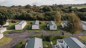 A row of small, single-story cabins with a grassy yard and a dirt path in between. - 'Serenity' A Tranquil & Peaceful Retreat set in a Cornish country park (Relubbus)
