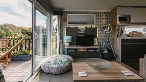 A modern kitchen with a flat-screen TV, a dining area with a wooden table, and a balcony with a wooden chair. - 'Serenity' A Tranquil & Peaceful Retreat set in a Cornish country park (Relubbus)
